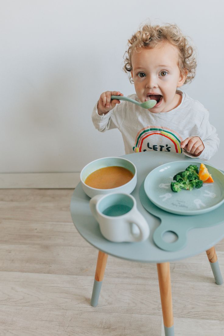 a child eating porridge made of vegetables, broccoli and an orange